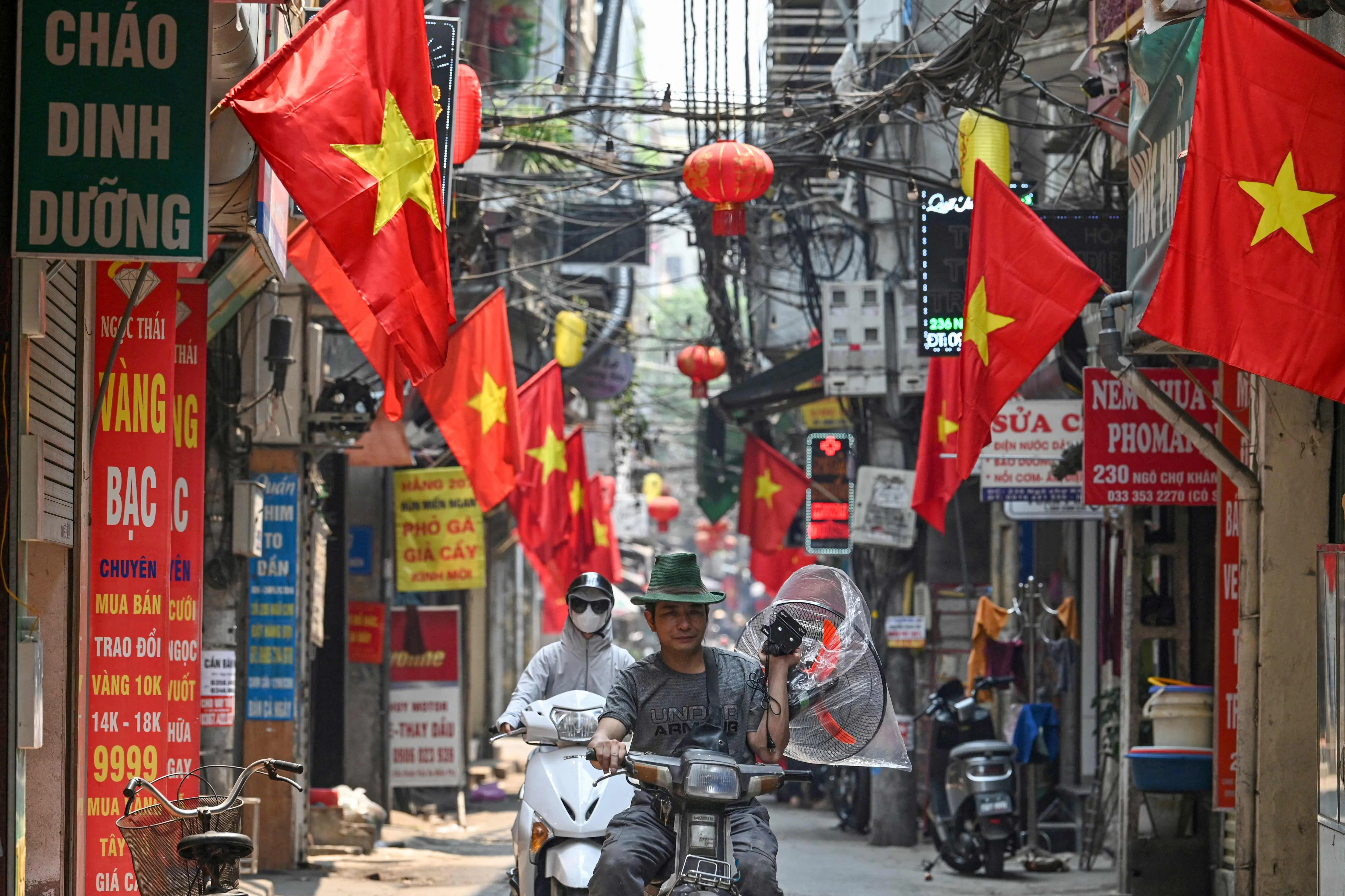 A man rides a motorbike along a street lined with Vietnamese national flags in Hanoi on 30 April 2024.