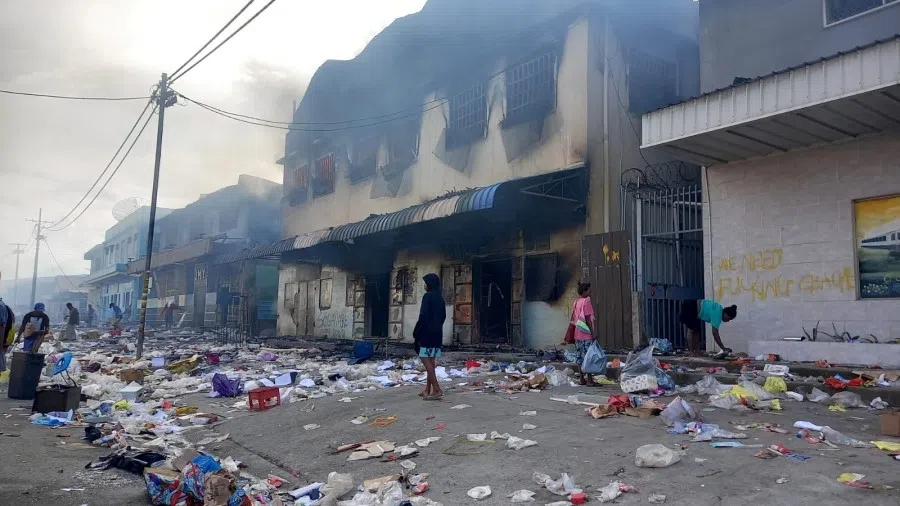 People stand amid debris in front of a burned-out building after days of unrest in Honiara, Solomon Islands, 26 November 2021. (Elizabeth Osifelo/Reuters)
