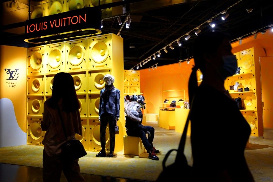 Customers wearing face masks following the Covid-19 outbreak walk past a store of French luxury brand Louis Vuitton inside a shopping mall in Beijing, China, 19 September 2020. (Tingshu Wang/Reuters)