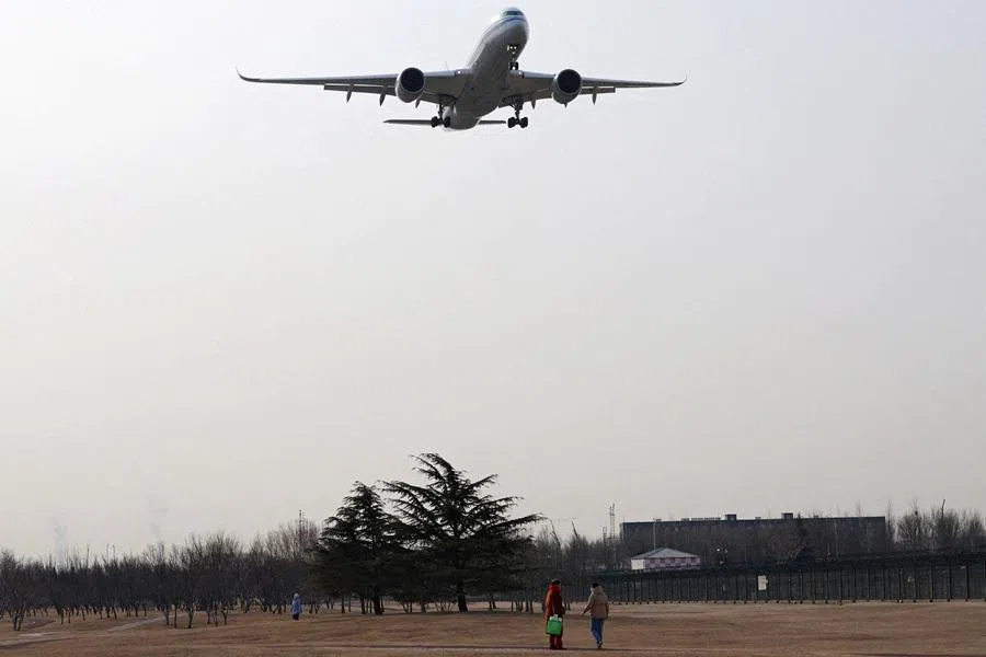 An aircraft flies above visitors at a park near the Beijing Capital International Airport, in Beijing, China, on 2 February 2024. (Florence Lo/Reuters)