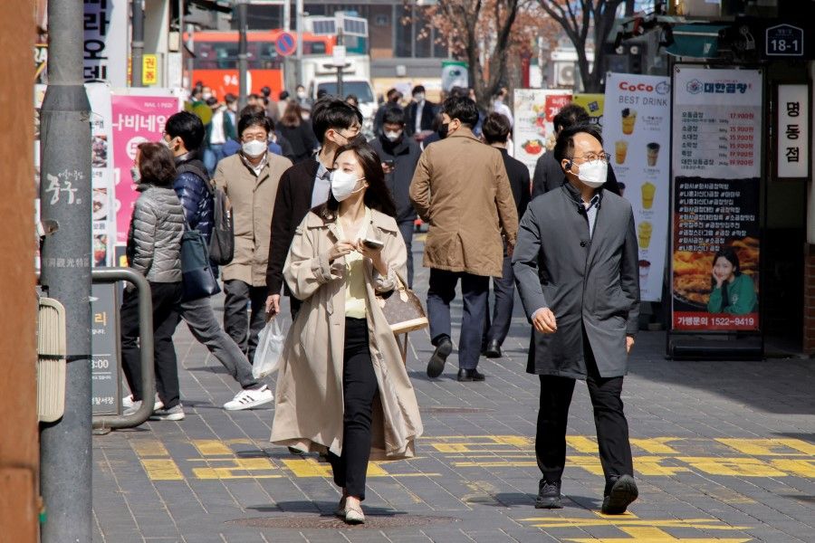 People wearing masks walk in a shopping district amid the Covid-19 pandemic in Seoul, South Korea, 16 March 2022. (Heo Ran/Reuters)