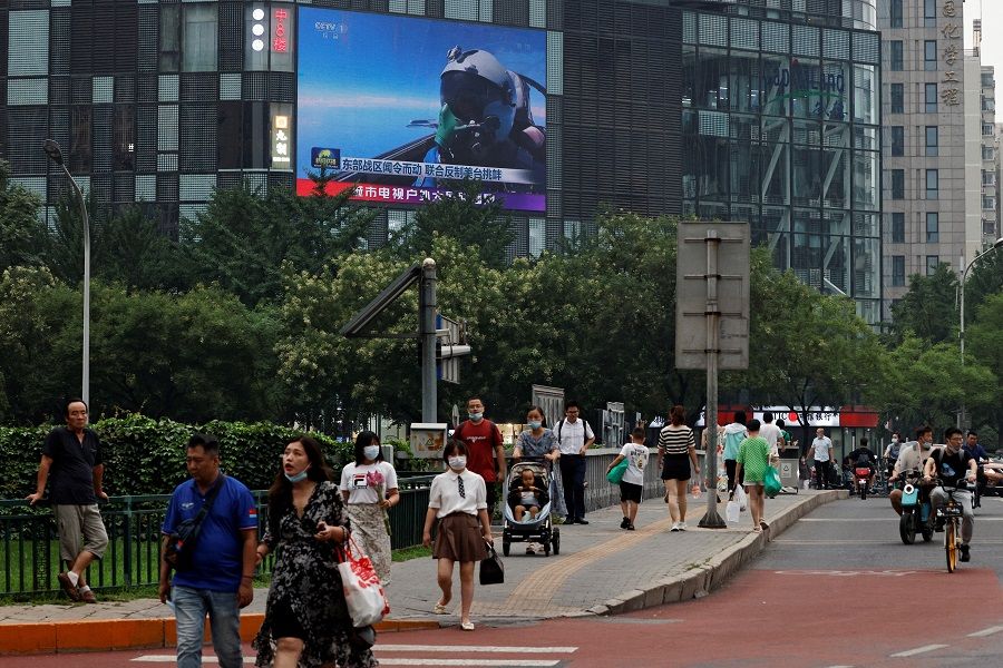 Pedestrians walk past a giant screen broadcasting a news report on the Chinese People's Liberation Army's (PLA) military exercises around Taiwan, in Beijing, China, 4 August 2022. (Thomas Peter/Reuters)