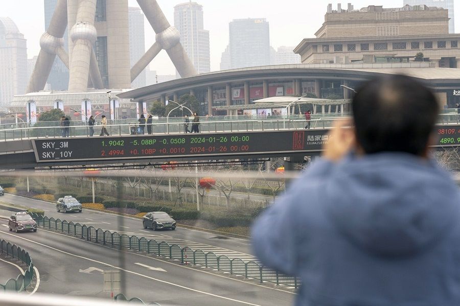 A man taking a picture with an electronic ticker displaying stock figures in the background, in Pudong's Lujiazui Financial District in Shanghai, China, on 29 January 2024. (Raul Ariano/Bloomberg)