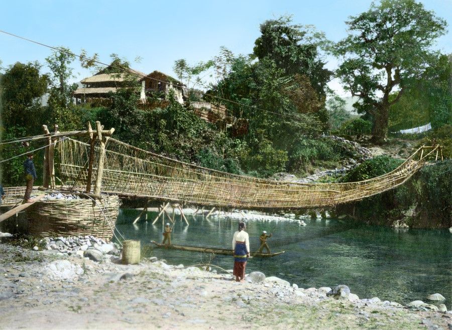 A rope suspension bridge in the mountains of Vietnam, 1920s. Under the bridge, boatmen row a light vessel.