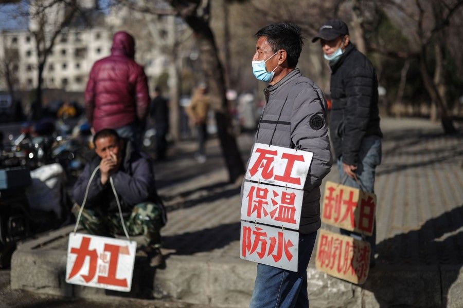 Day labourers wearing face masks hold signs advertising their skills as they wait to get hired for renovation works in Shenyang in China's northeastern Liaoning province, 27 March 2020. (STR/AFP)