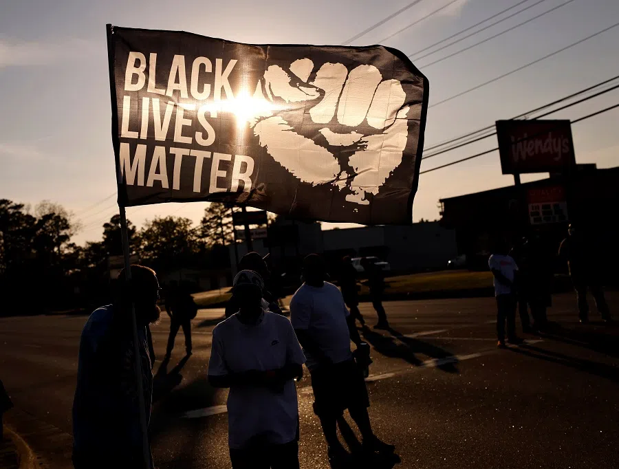 The setting sun shines through a Black Lives Matter flag as protesters occupy a busy intersection in Elizabeth City, North Carolina, US, on 28 April 2021. (Jonathan Drake/Reuters)