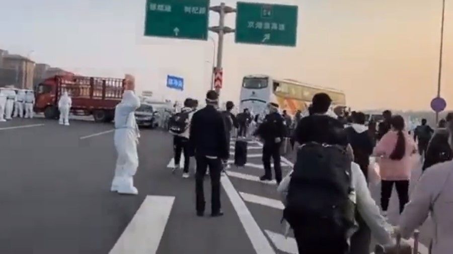 A screen grab from a video showing Foxconn workers running for a bus as health workers and police stand by. (Twitter)