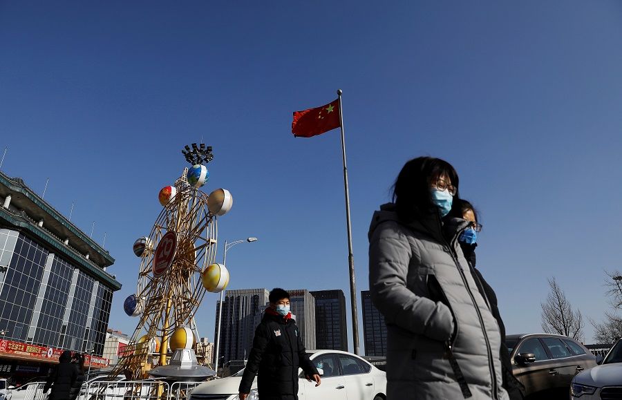 People wearing face masks walk past a Chinese flag in Beijing, China, 11 January 2021. (Tingshu Wang/Reuters)