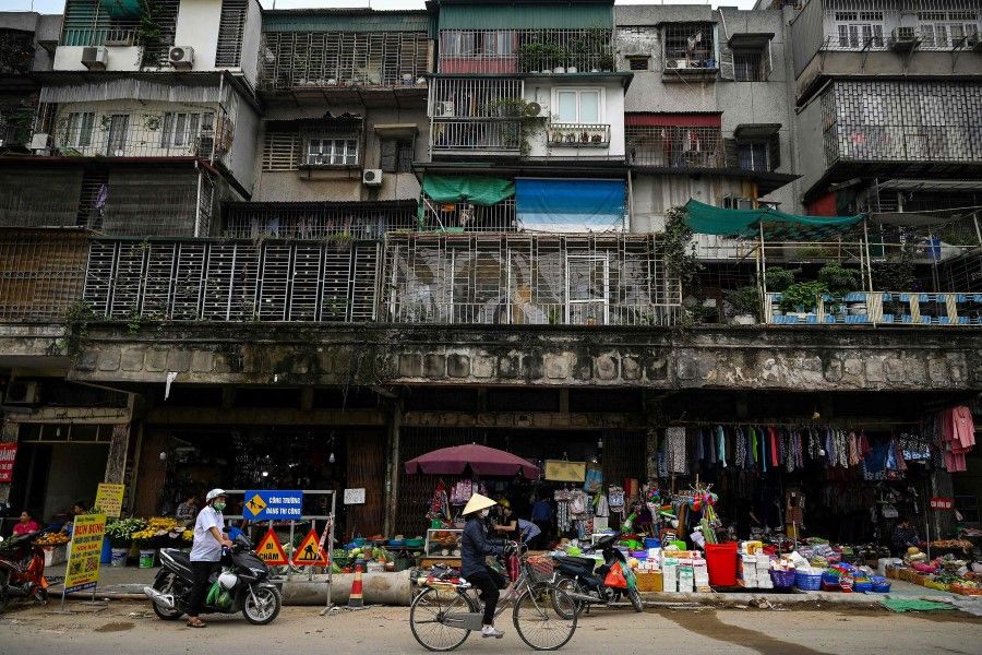 A woman rides her bicycle past shops beneath a residential building in Hanoi on 31 March 2021. (Manan Vatsyayana/AFP)