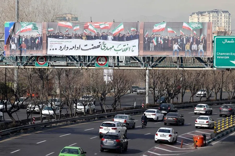 Vehicles drive along a highway under a pedestrian bridge with a huge banner showing people waving the Iranian flag, in Tehran on 18 February 2026. (Atta Kenare/AFP)