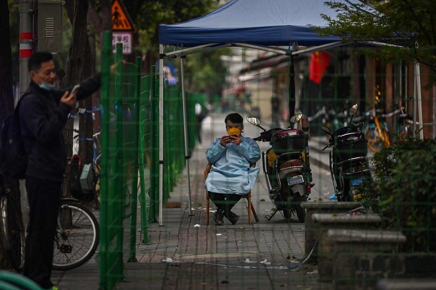 A guard is seen through a fence closing an area in lockdown in the Changning district, after new Covid-19 cases were reported in Shanghai, China, on 8 October 2022. (Hector Retamal/AFP)