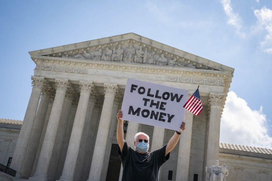 A demonstrator wearing a protective mask holds a "Follow The Money" sign outside the U.S. Supreme Court in Washington, 9 July 2020. The court cleared a New York grand jury to get President Donald Trump's financial records while blocking for now House subpoenas that might have led to their public release before the election. (Sarah Silbiger/Bloomberg)