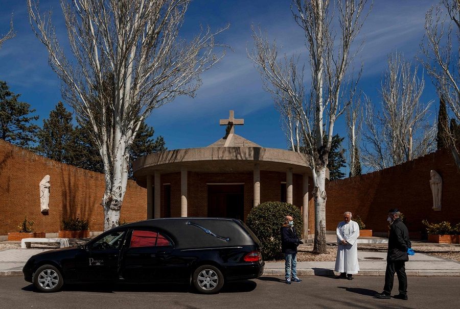 Mortuary employees wearing face masks stand next to a priest before the burial of a Covid-19 coronavirus victim at the Fuencarral cemetery in Madrid on 29 March 2020. (Baldesca Samper/AFP)