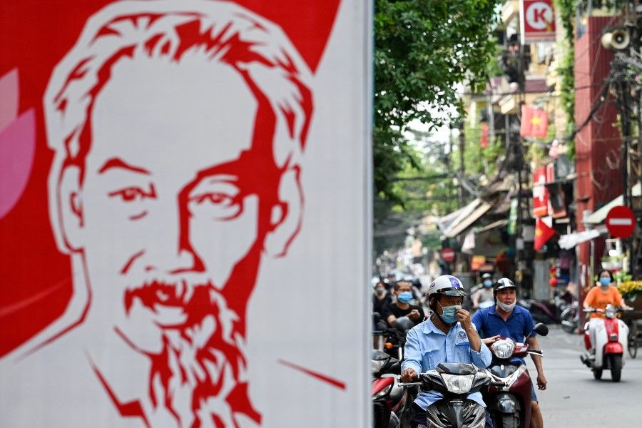 A man wearing a face mask amid Covid-19 concerns waits on his scooter near a billboard of the late Vietnamese revolutionary leader Ho Chi Minh, Hanoi, 4 May 2021. (Manan Vatsyayana/AFP)