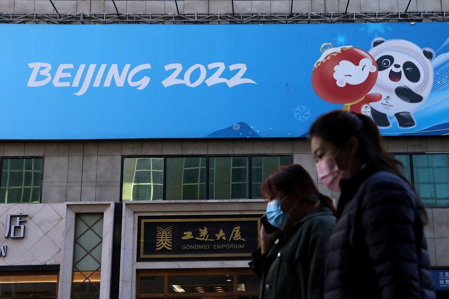 People walk past a banner with a sign of Beijing 2022 Winter Olympic Games, in Beijing, China, 27 October 2021. (Tingshu Wang/File Photo/Reuters)