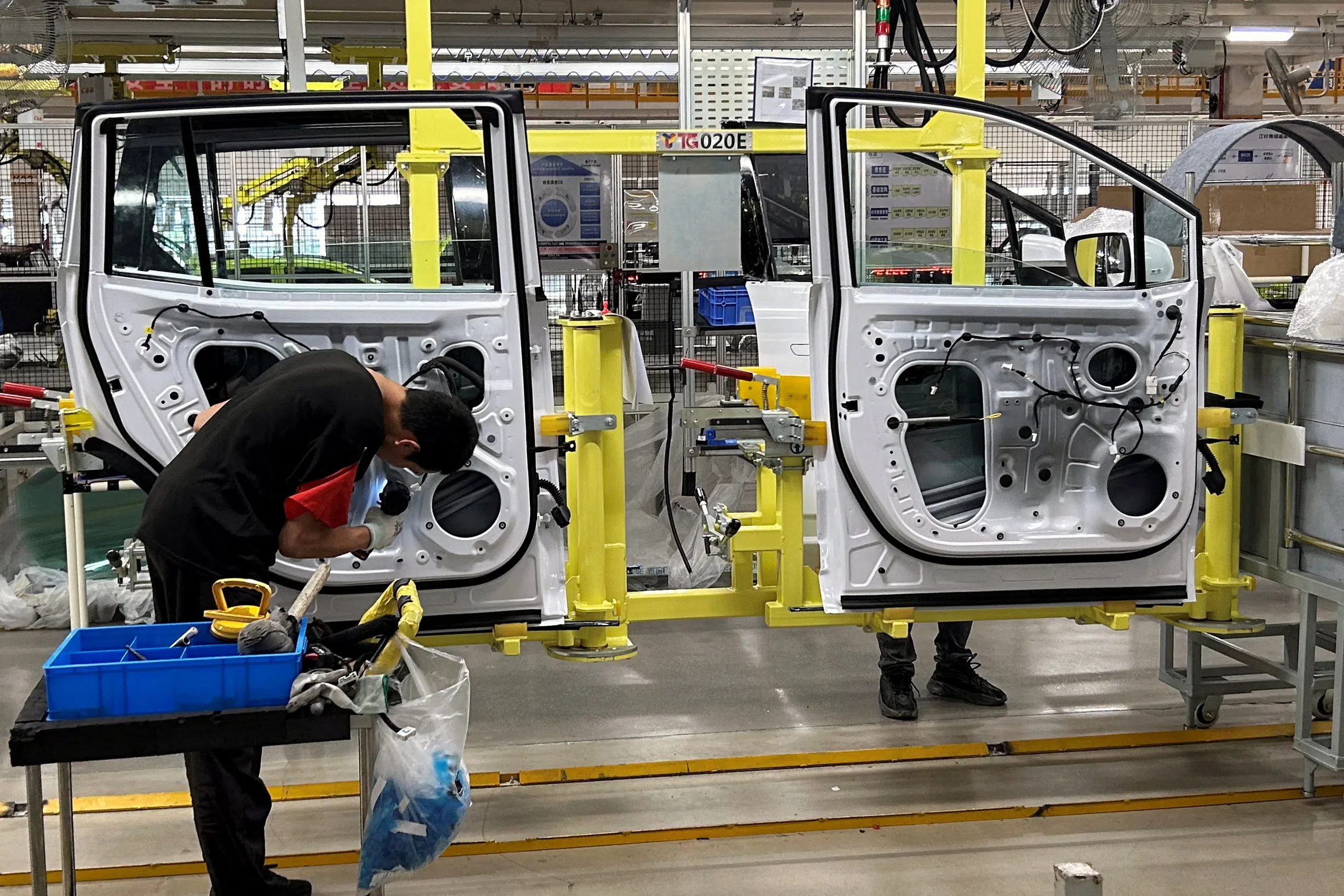 Employees work on an electric vehicle (EV) production line in a factory under Jiangling Group Electric Vehicle (JMEV) in Nanchang, Jiangxi province, China, on 22 May 2024. (Kevin Krolicki/Reuters)