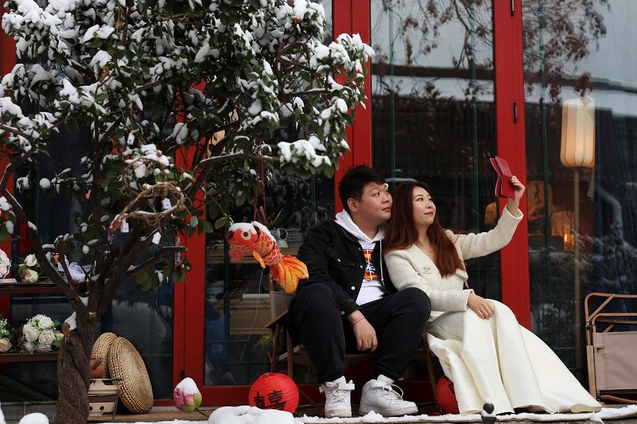 A couple poses with their marriage certificate during a photo shooting session on a snowy day in Beijing, China, on 11 December 2023. (Tingshu Wang/Reuters)