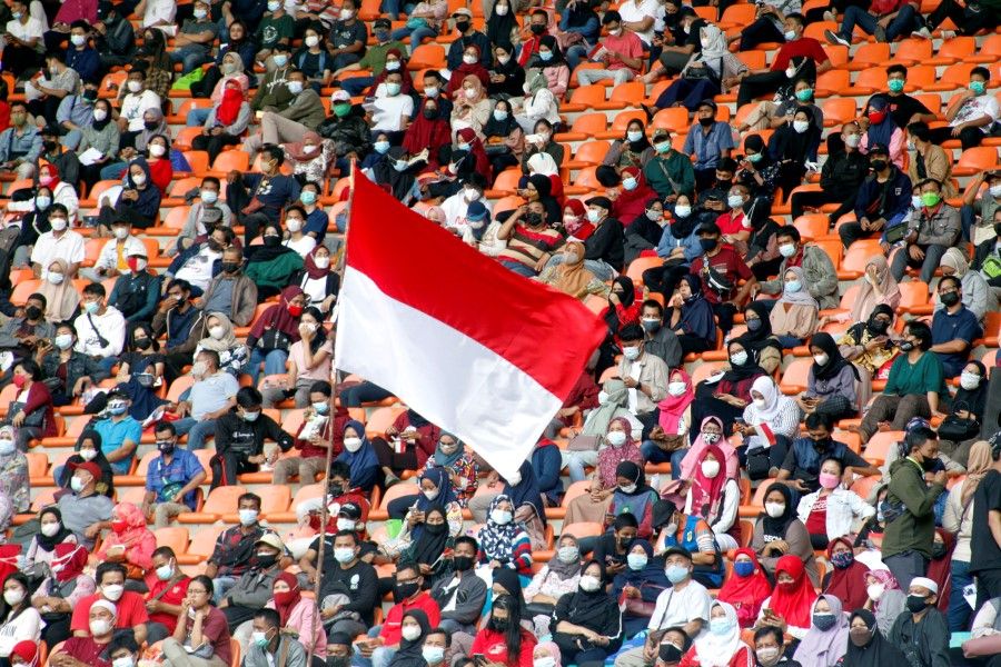 The Indonesian flag flies as people wearing protective face coverings wait to receive a coronavirus disease (COVID-19) vaccine dose at Pakansari Stadium in Bogor, on the outskirts of Jakarta, Indonesia, 14 August 2021. (Yulius Satria Wijaya via Reuters)