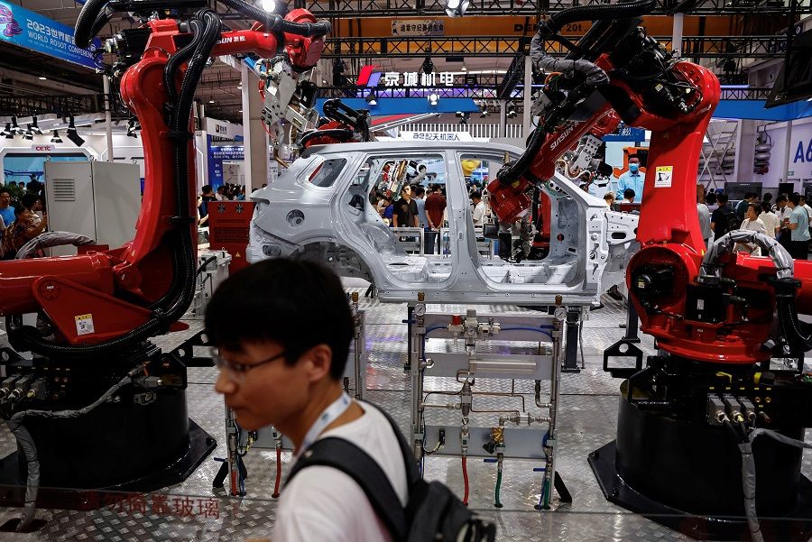 A visitor stands near robotic welding arms used in car production developed by Siasun, at the World Robot Conference 2023 in Beijing, China, 17 August 2023. (Tingshu Wang/Reuters)