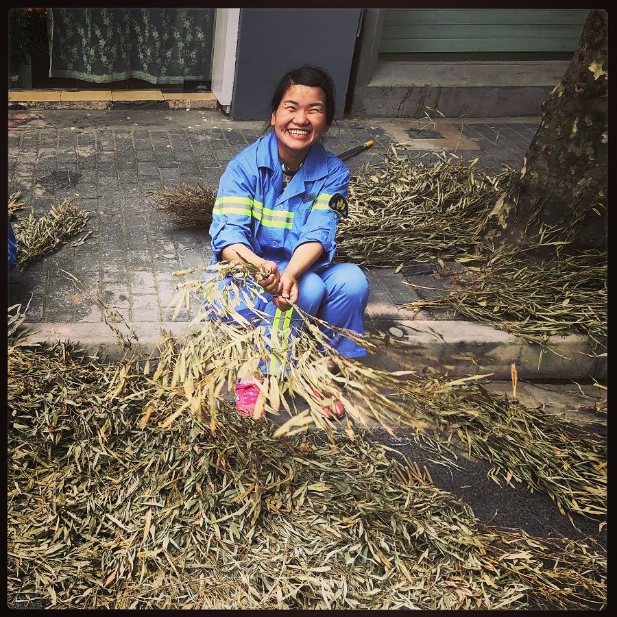 A street sweeper with a disarming smile takes a break from cleaning the streets of Huangpu, Shanghai to fix her straw broom.