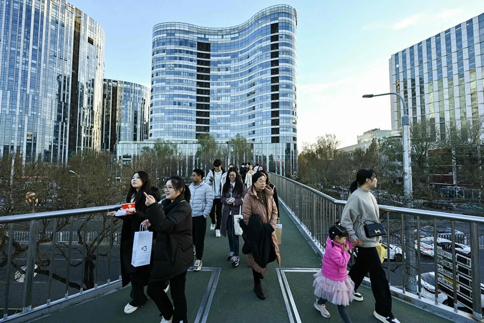 People walk along an overpass at the Sanlitun business area in Beijing, China, on 30 November 2024. (Adek Berry/AFP)