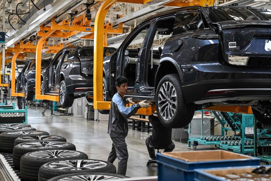 An employee places side molding on a car along the assembly line at a factory of Chinese automaker NIO in Hefei, in China's eastern Anhui province on 10 May 2023. (Hector Retamal/AFP)