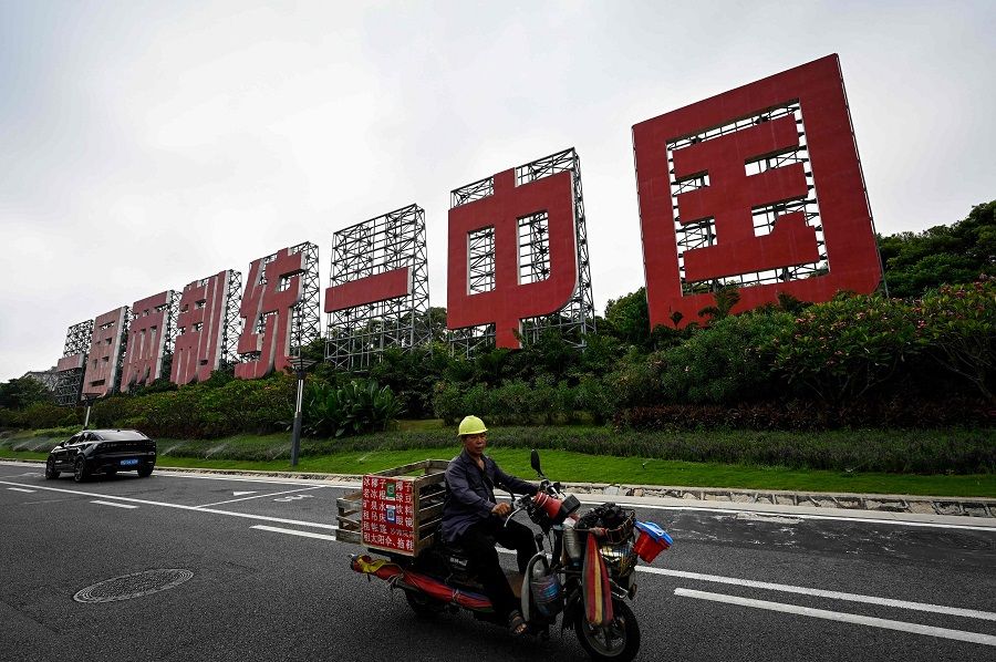 This photo taken on 25 July 2022 shows a man riding past a giant sign proclaiming "One Country, Two Systems, Unify China" in Xiamen, Fujian province, China. (Jade Gao/AFP)