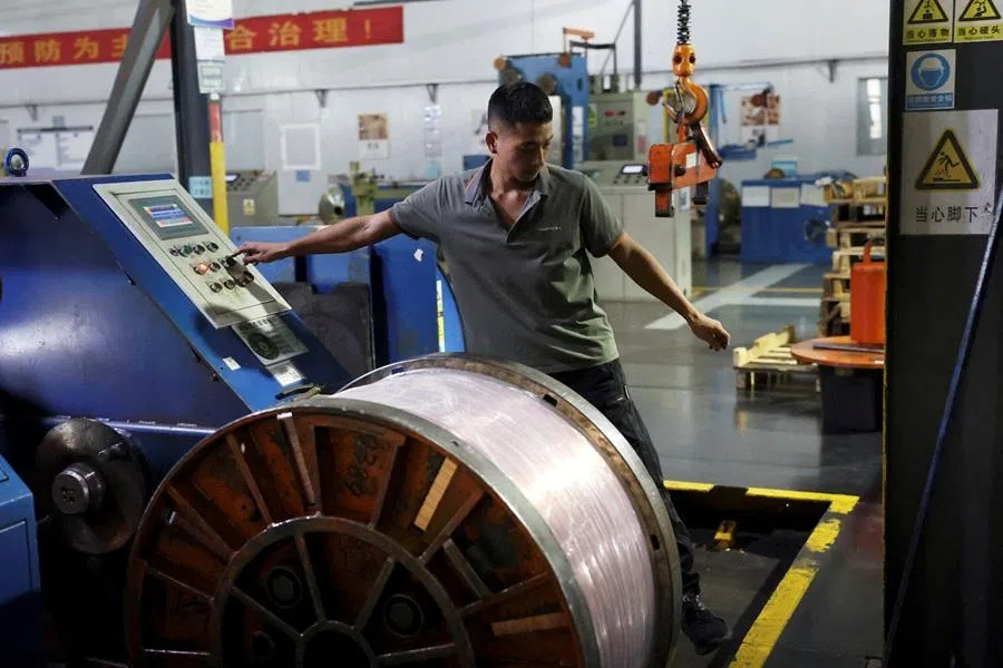 An employee works next to a reel of copper flat wire on the production line at a factory in Ganzhou, Jiangxi province, China, on 14 August 2025. (Florence Lo/Reuters)