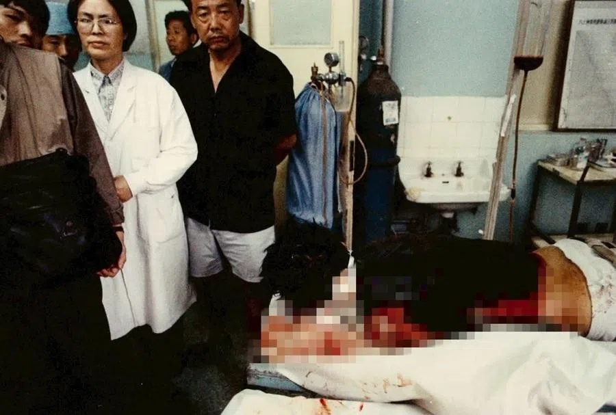 After I was shot, I was rushed to Tongren Hospital, where photographer Xu Yong captured this photograph of me lying in bed. The man in the black shirt is the one who saved my life. (Image pixelated for graphic content.)