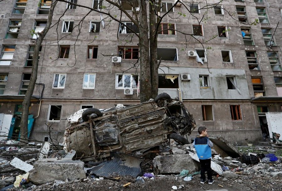 A boy stands next to a wrecked vehicle in front of an apartment building damaged during the Russia-Ukraine conflict in the southern port city of Mariupol, Ukraine, 24 April 2022. (Alexander Ermochenko/Reuters)