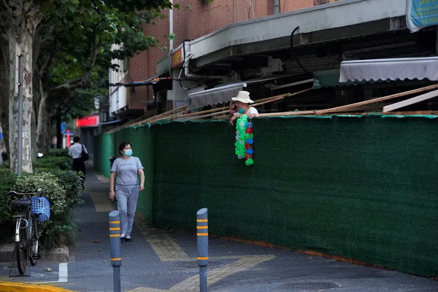 A man talks on a phone behind a barrier of a sealed area, in Shanghai, China, 11 July 2022. (Aly Song/Reuters)