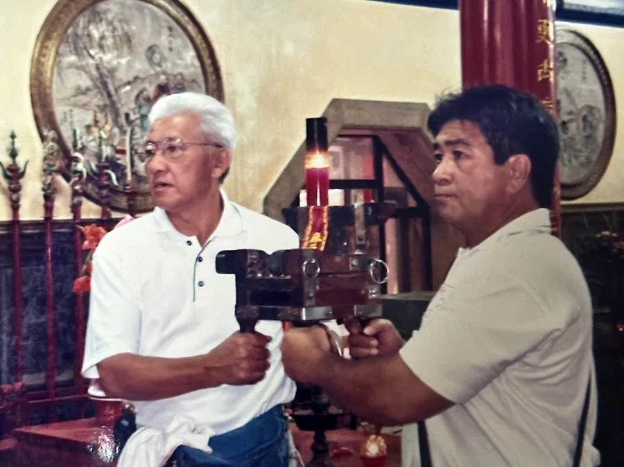 My father (left) holding one side of the spirit-medium chair during a temple service, Brunei, 2000s.