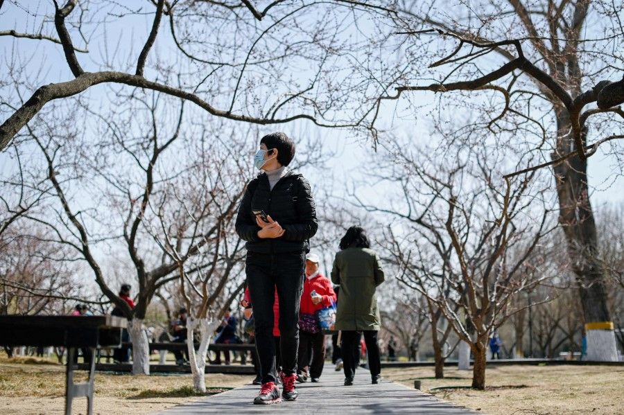 People walk in a public park under blue skies in Beijing on 16 March 2021. (Wang Zhao/AFP)