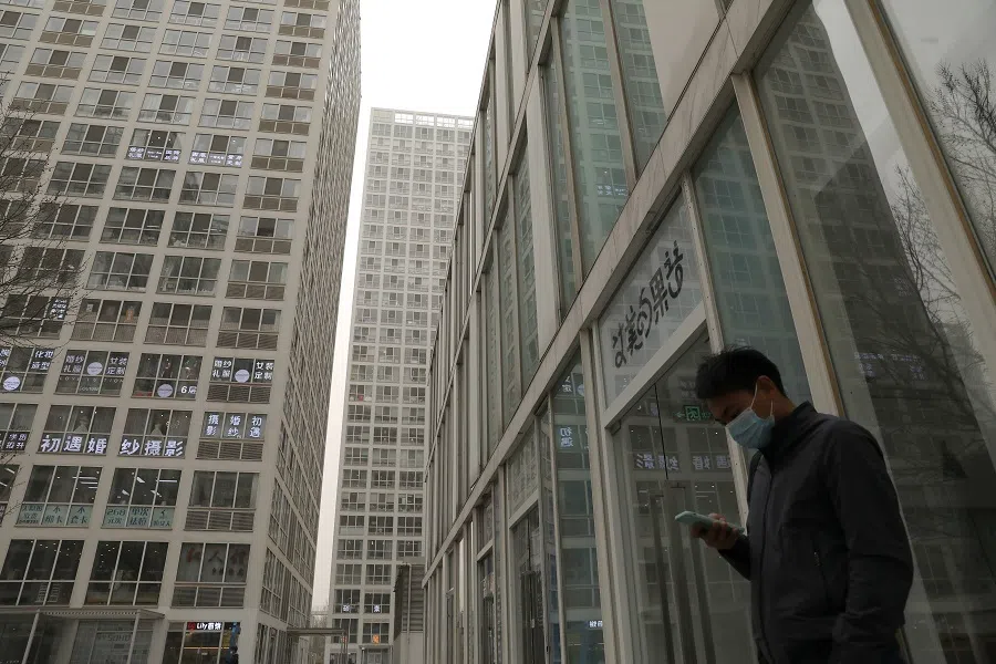 A man wearing a face mask checks his phone at an office and commercial complex in Beijing's central business district, China, 15 March 2021. (Tingshu Wang/Reuters)