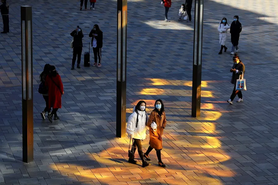 People wearing face masks walk at a shopping complex in Beijing, China, 1 December 2021. (Tingshu Wang/Reuters)