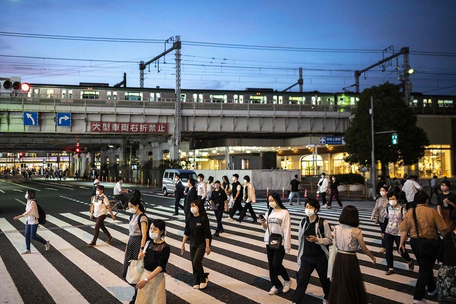 People cross a street at dusk in Tokyo, Japan, on 5 October 2021. (Charly Triballeau/AFP)