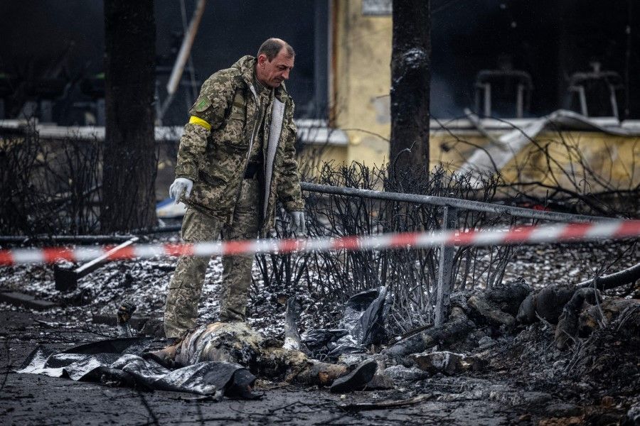 A police officer examines the bodies of passersby killed in yesterday's airstrike that hit Kyiv's main television tower in Kyiv on 2 March 2022. (Photo by Dimitar Dilkoff/AFP)