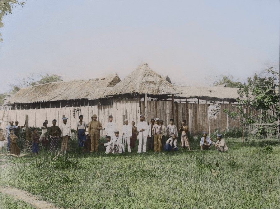 A German manager with Malay workers. The German security personnel with guns have come off a boat. The large straw building in the photograph is mainly used for storage and work lodgings. One can see the relationship between Western traders and coolie employers.
