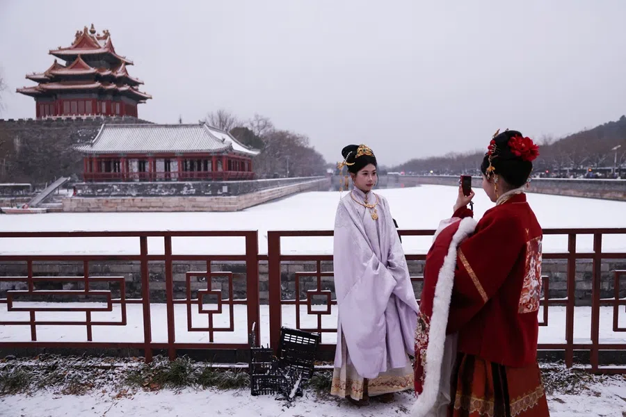 A woman dressed in a traditional costume poses for pictures amid snowfall near a corner tower of the Forbidden City, in Beijing, China, 12 December 2025. (Tingshu Wang/Reuters)