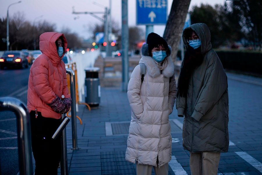 Women wearing face masks stand at a bus station on a cold winter day in Beijing on 29 December 2020. (Wang Zhao/AFP)