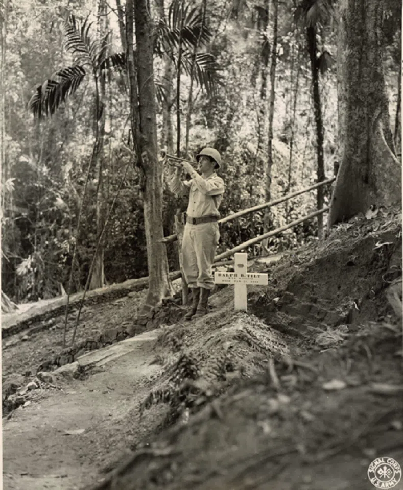 A photograph taken by Tom Amer on 30 May 1944, of George W. Arkle playing “Taps” over the grave of Major Ralph B. Tilt, who was killed in action in Burma. This cemetery is the first official American Military Cemetery in Burma at Shingbwiyang in northern Burma.