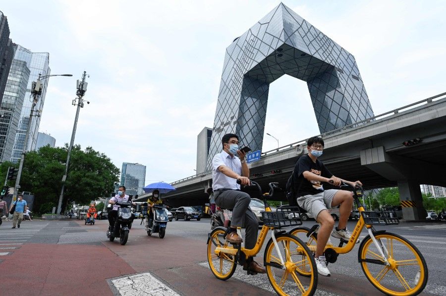 People ride bicycles along a street at a Central Business District in Beijing on 8 July 2022. (Wang Zhao/AFP)