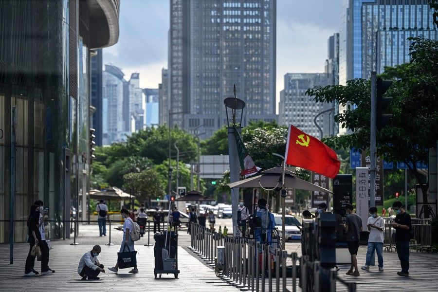 This photo taken on 8 July 2022, shows people passing a checkpoint with a flag of the Chinese Communist Party at a shopping mall in Shenzhen, in China's southern Guangdong province. (Jade Gao/AFP)