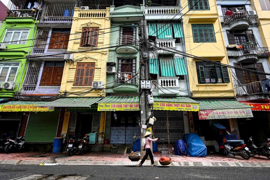 This photograph taken on 8 June 2021 shows a street vendor walking past narrow residential houses, known as "nha ong" in Vietnamese or "tube houses", in an urban area of Hanoi. (Manan Vatsyayana/AFP)