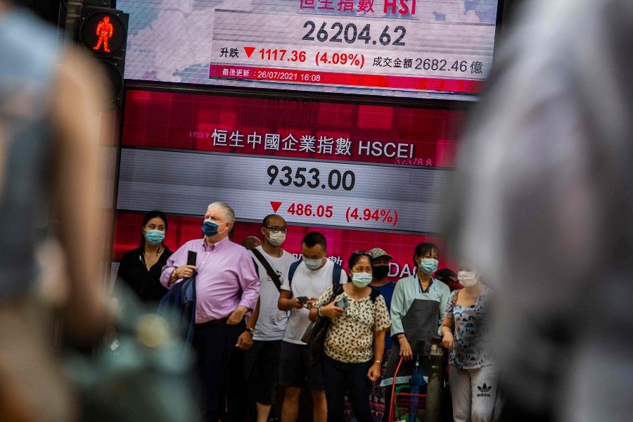 People stand in front of an electronic display showing the Hang Seng Index in the Central district of Hong Kong on 26 July 2021. (Isaac Lawrence/AFP)