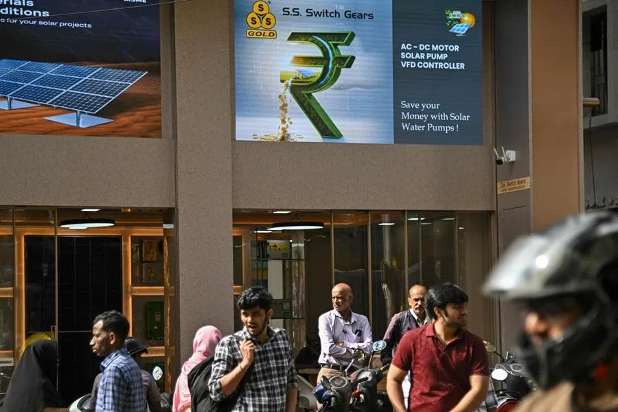 Pedestrians wait below a digital advertisement featuring the Indian rupee symbol at Chickpet market in India on 26 December 2025. (Idrees Mohammed/AFP)