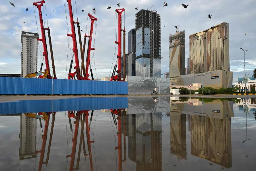 A cyclist (centre) rides past high-rise buildings under construction in Phnom Penh on 16 July 2021. (Tang Chhin Sothy/AFP)