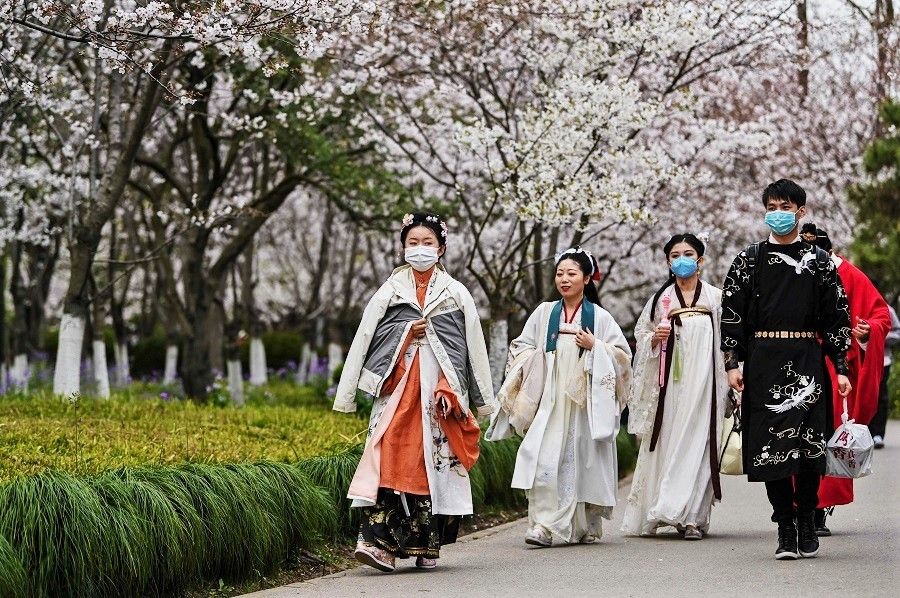 Young people wearing face masks amid concerns over the Covid-19 coronavirus walk dressed in Tang Dynasty costumes at Century Park in Shanghai on 22 March 2020. (Hector Retamal/AFP)