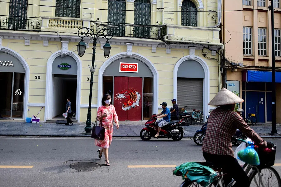 A woman (centre) crosses a street as traffic goes past in Hanoi, Vietnam, on 25 May 2023. (Manan Vatsyayana/AFP)