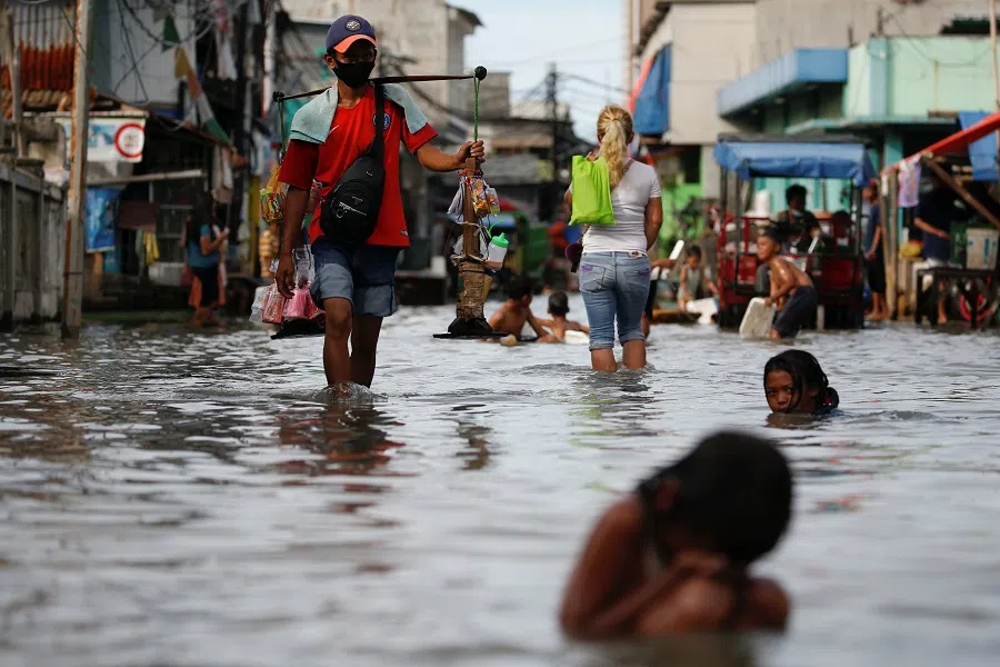 A street vendor walks through water in a densely populated area that floods due to high tides, in Muara Angke district in Jakarta, Indonesia, 9 November 2021. (Willy Kurniawan/Reuters)